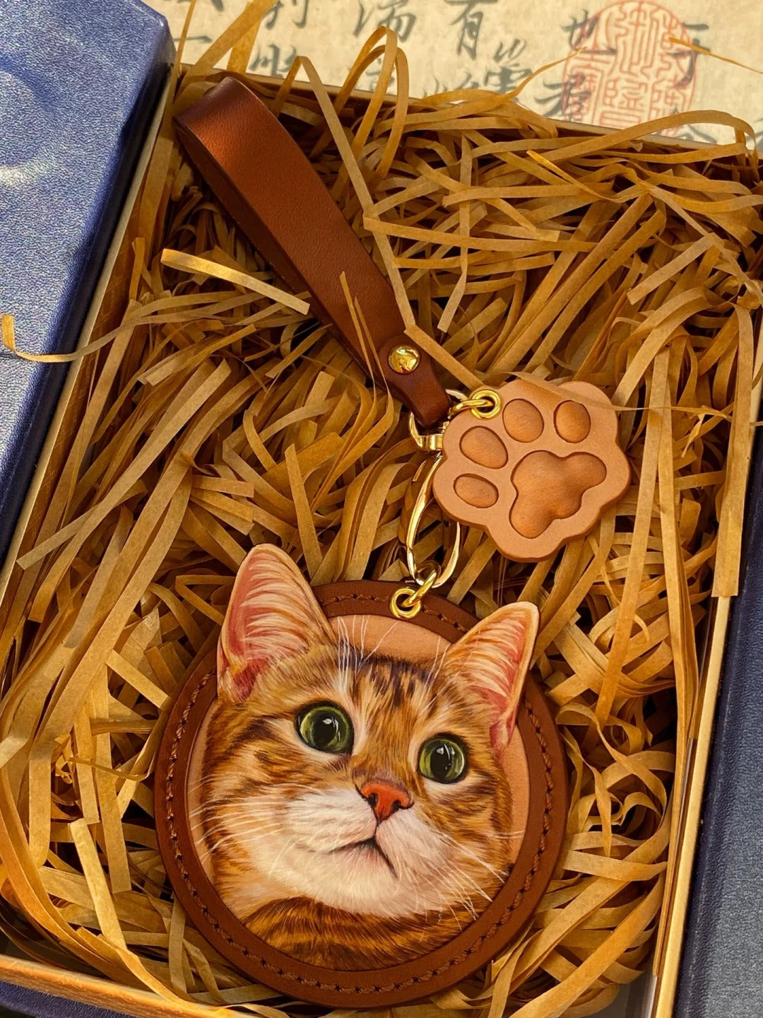 Custom leather portrait charm of a tabby cat with green eyes, packed in gift box with matching brown paw tag and leather strap