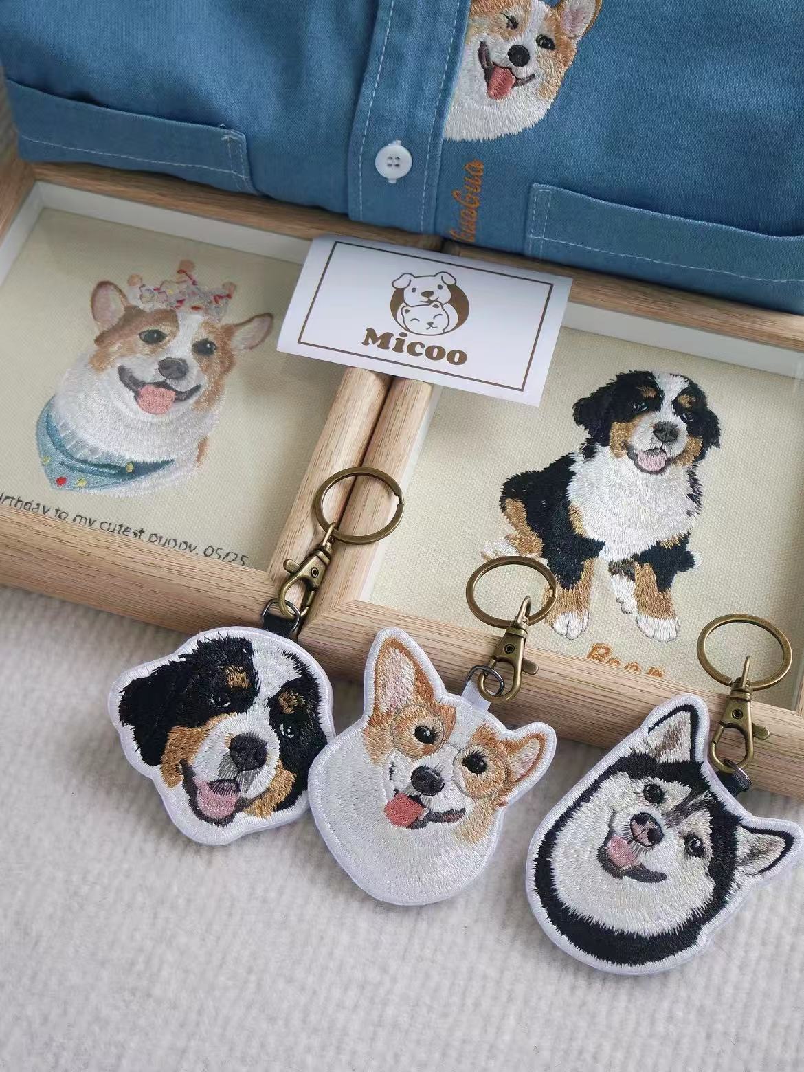 Three embroidered dog keychains with happy expressions, placed beside custom dog artwork and denim shirt embroidery.