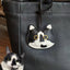 Realistic black and white cartoon cat charm hanging on a black leather bag, custom pet portrait made from goatskin leather

