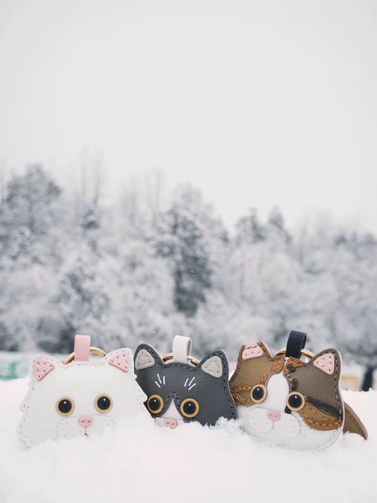 Trio of personalized cartoon pet leather charms in snow, showing white, gray, and brown cats, custom from real pet photos