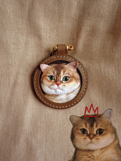 Realistic leather pet portrait charm of a British Shorthair cat in a stitched round brown frame with gold rivet, based on real photo