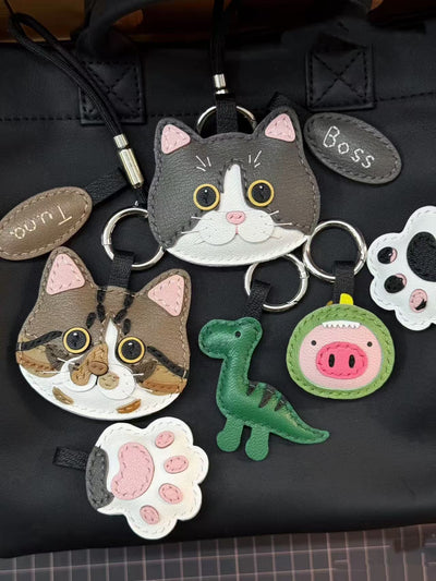 Multiple custom pet leather hanging charms with cat faces, paw tags, and animal add-ons, made from goatskin leather with name tag options