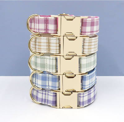 Stack of plaid pet collars in pink, beige, green, blue, and purple with gold buckles.