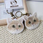 Pair of personalized embroidered round-face cat keychains with antique brass rings on beige fabric.