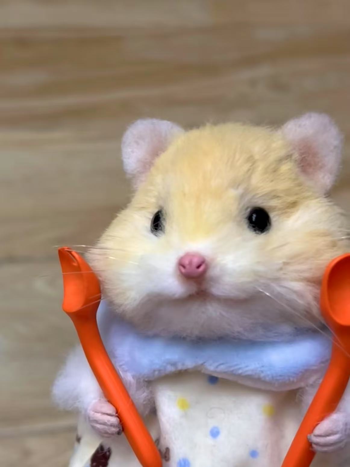 Handmade twist yarn stick of a light brown hamster holding orange spoons