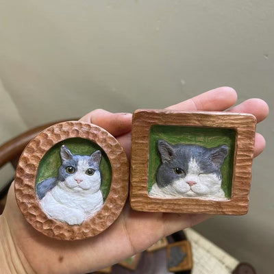 One round with a hammered texture, the other square with a rough-hewn frame, both featuring hand-painted gray and white cats with green backgrounds.