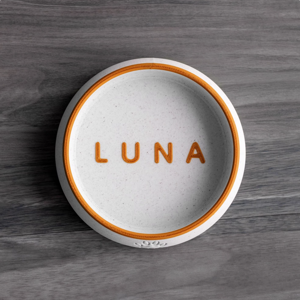 White PLA pet bowl with orange rim and engraved name “LUNA”